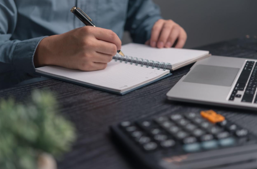 Person managing betting bankroll on laptop and notebook in a calm focused workspace